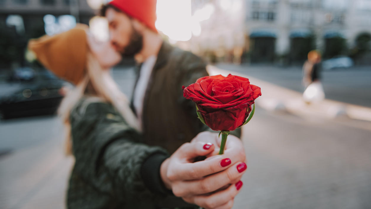Valentinstag: Blumen verschicken – letzte Chance für Rosen und Sträuße Mann küsst Frau und schenkt ihr eine Rose.