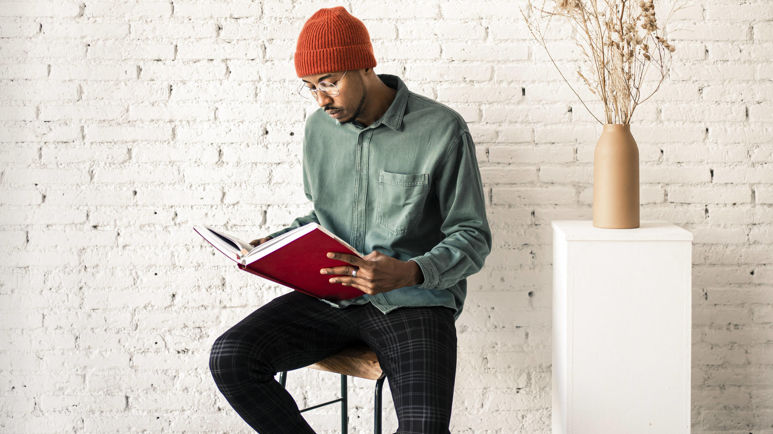 Diese 3 Trends trägt Man(n) im Frühling 2021 Man in knit hat reading book by dried plant vase against white brick wall model released Symbolfoto property released RCPF00507