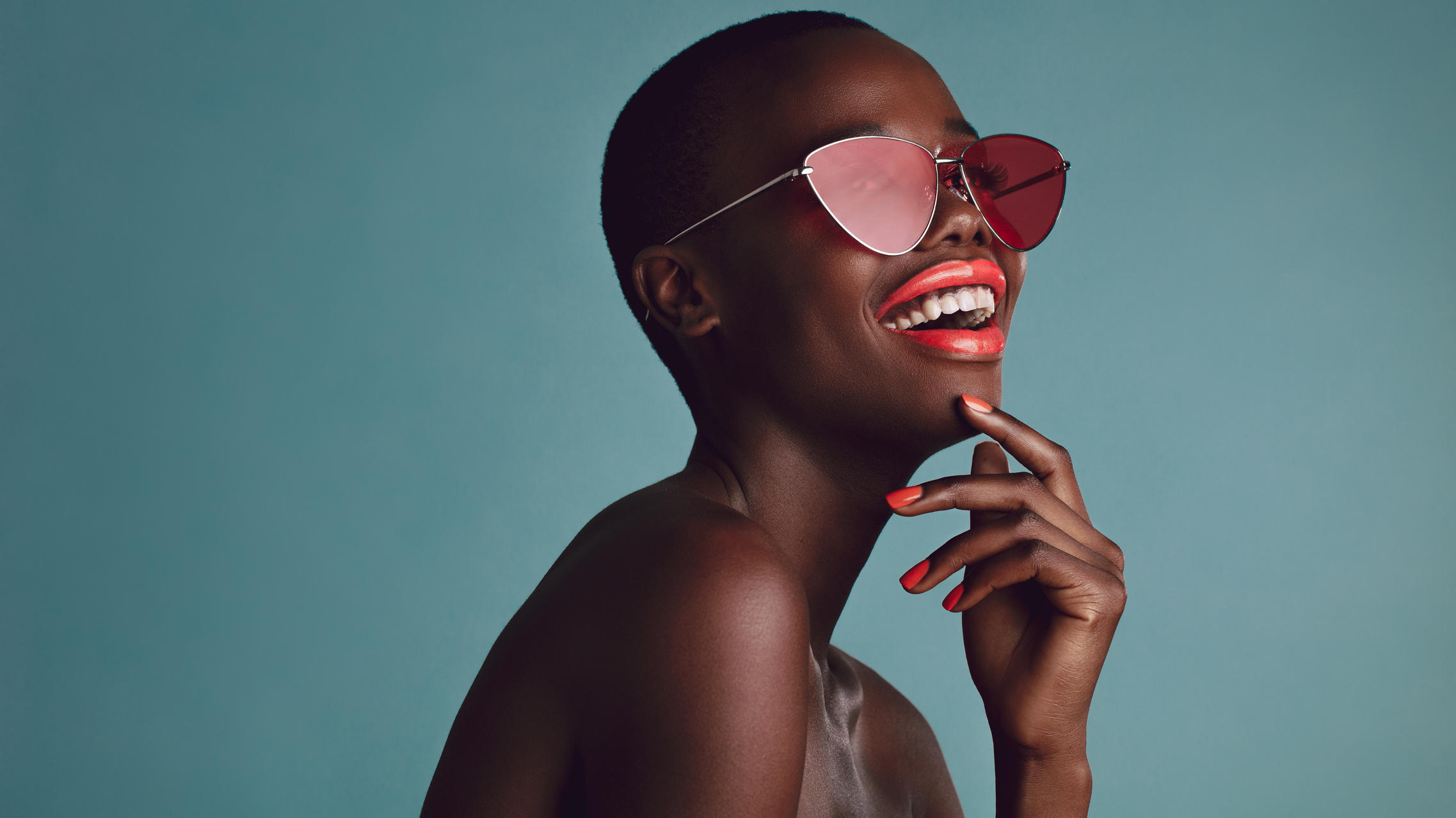 Diese 3 Sonnenbrillen-Trends sollte 2021 jeder kennen Schöne Frau mit Sonnenbrille vor blauem Hintergrund lacht.