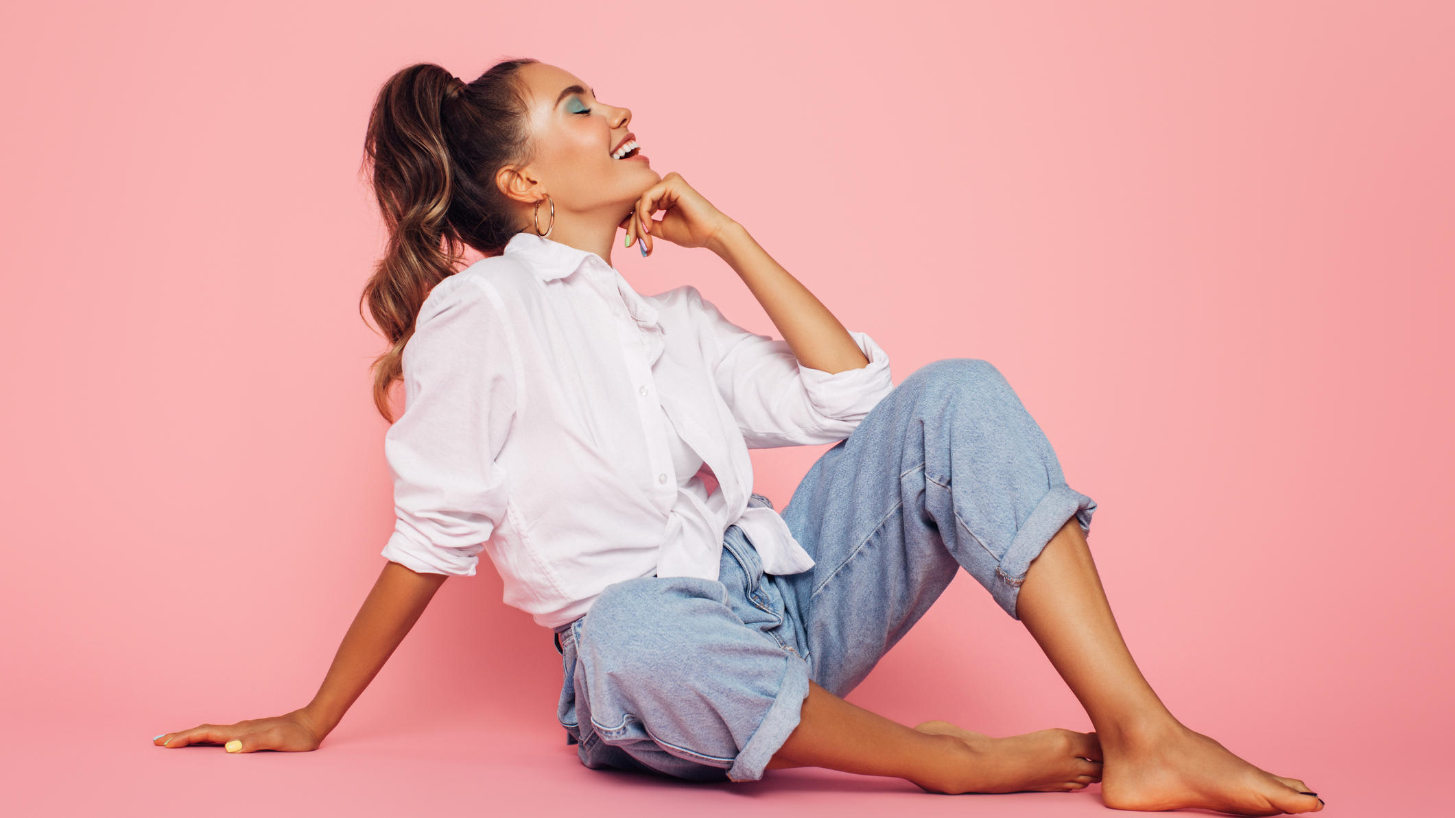 Jeans-Trends: Diese Hosen-Styles schmeicheln allen Frauen Frau auf dem Boden vor pinkem Hintergrund.