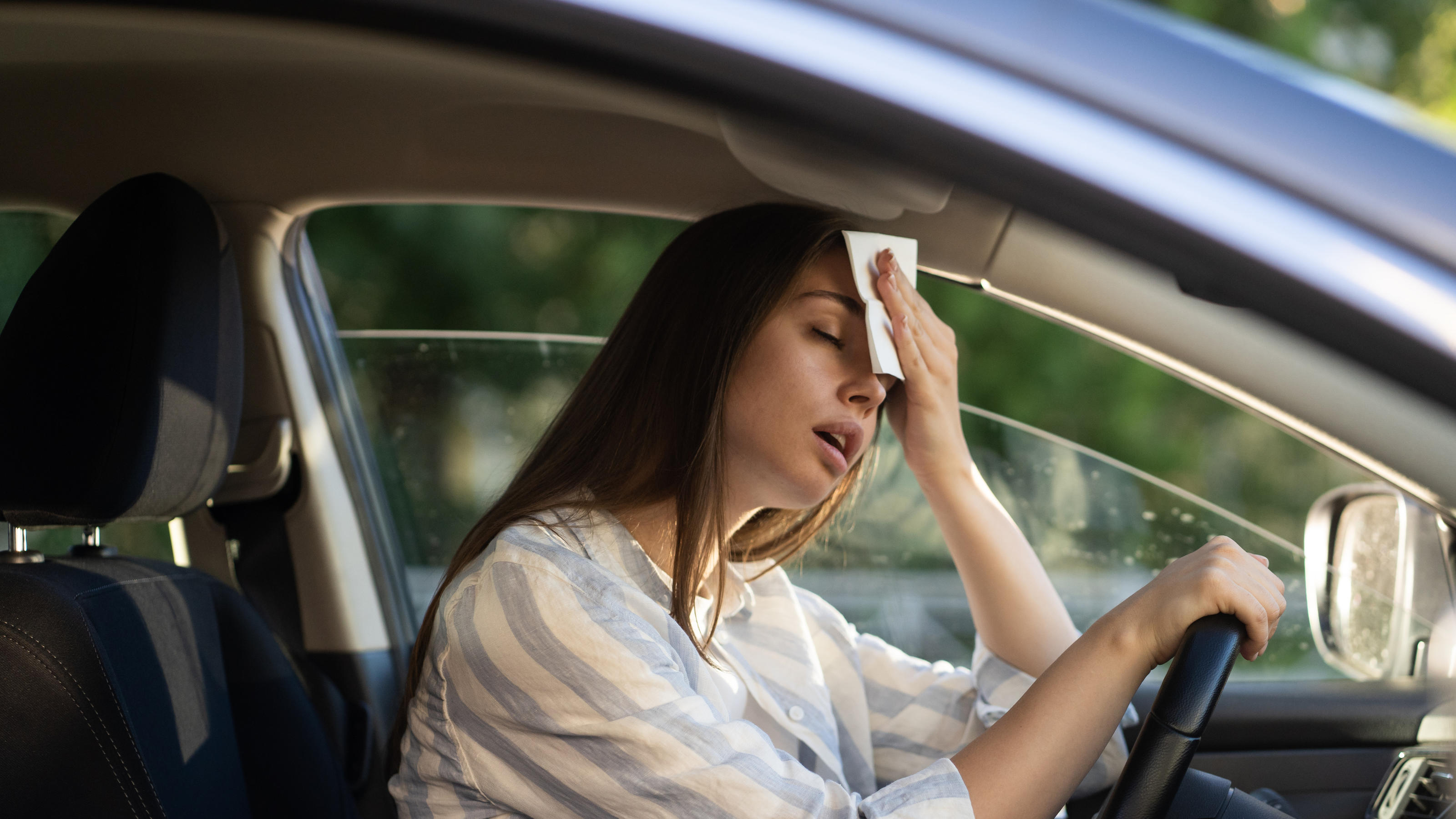 Mit dem Auto durch die Hitze: Cooles Kfz-Zubehör Eine Frau im Auto die sich an den Kopf fasst, weil es zu heiß ist.