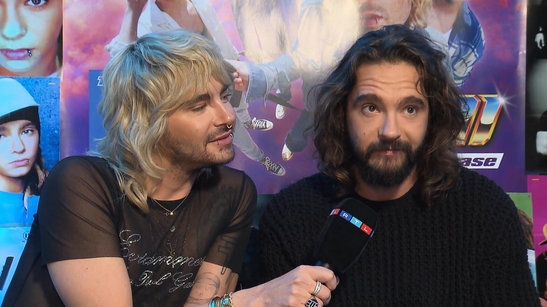 Bill und Tom Kaulitz im RTL-Interview. Bill lehnt sich zu Tom herüber und schaut ihn an, Tom hält ein Mikro in der Hand und guckt schüchtern nach oben.